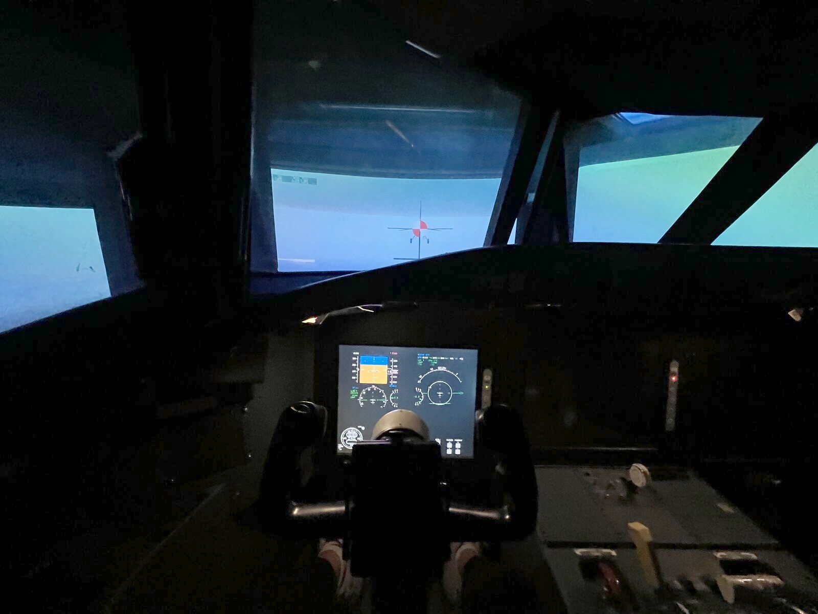 The UTIAS flight research simulator cab from the pilot's seat: out-the-window visual with a target aircraft ahead, a lit glass PFD and MFD on the centre console, the yoke in the foreground and the throttle quadrant to the right.