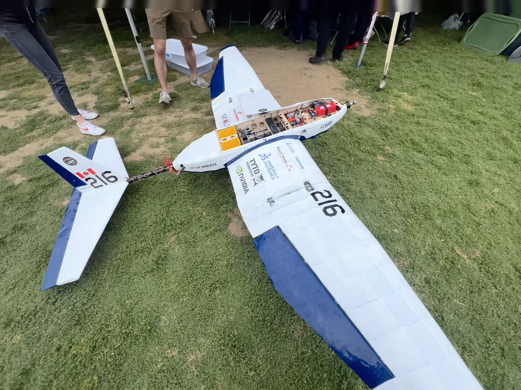 A different competition aircraft on grass, seen from above and behind: blue and white, single nose engine, the number 216 on the wing and on the fin, UT-24 MINERVA lettered on the fuselage, tail assembly detached and the equipment bay open.