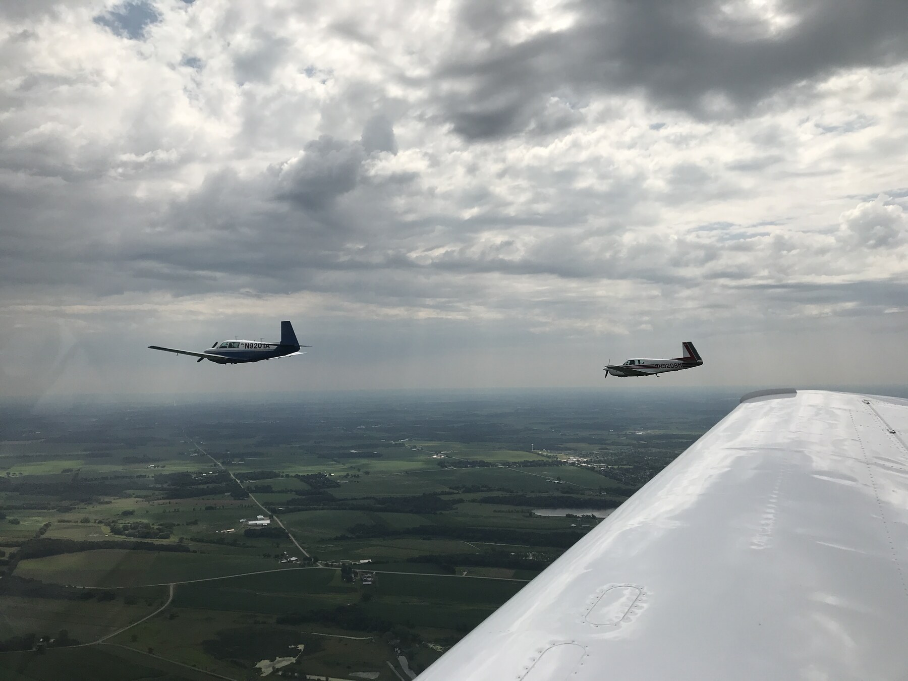 Two Mooneys in echelon formation, own wing visible from the cockpit