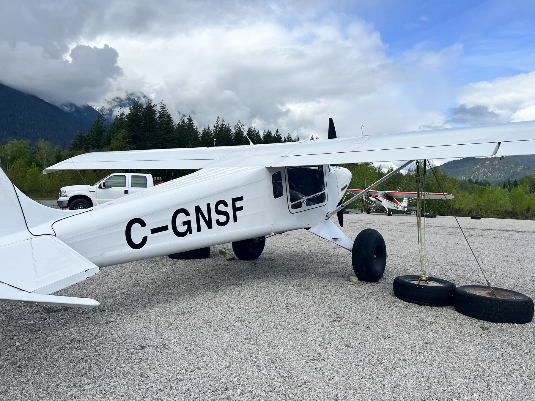C-GNSF on gravel at Squamish, wing and strut close to the camera, forested mountains behind.