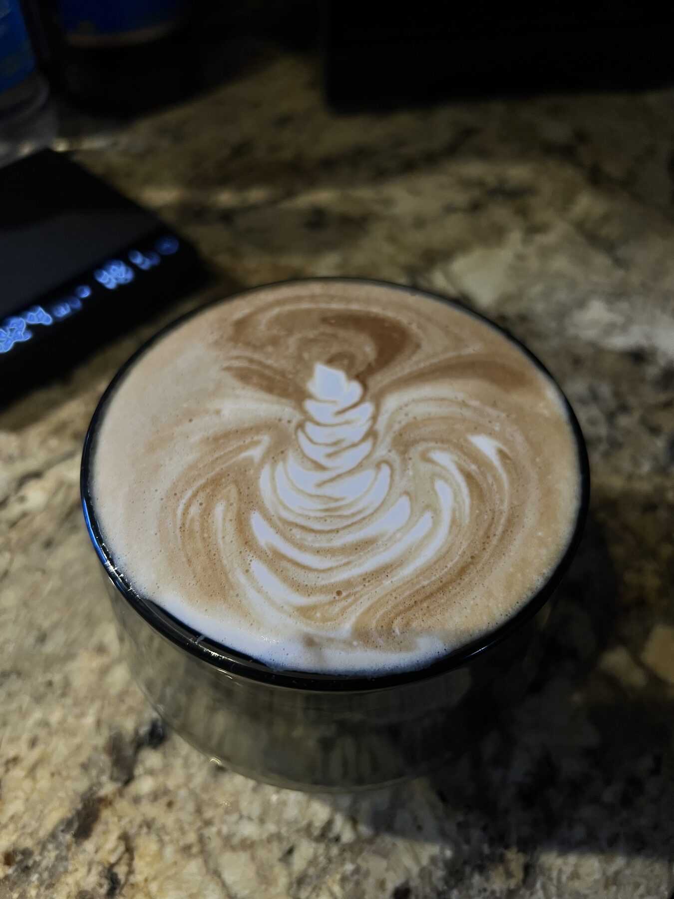 High-contrast spiral pour in a thick glass cup, scale visible behind.