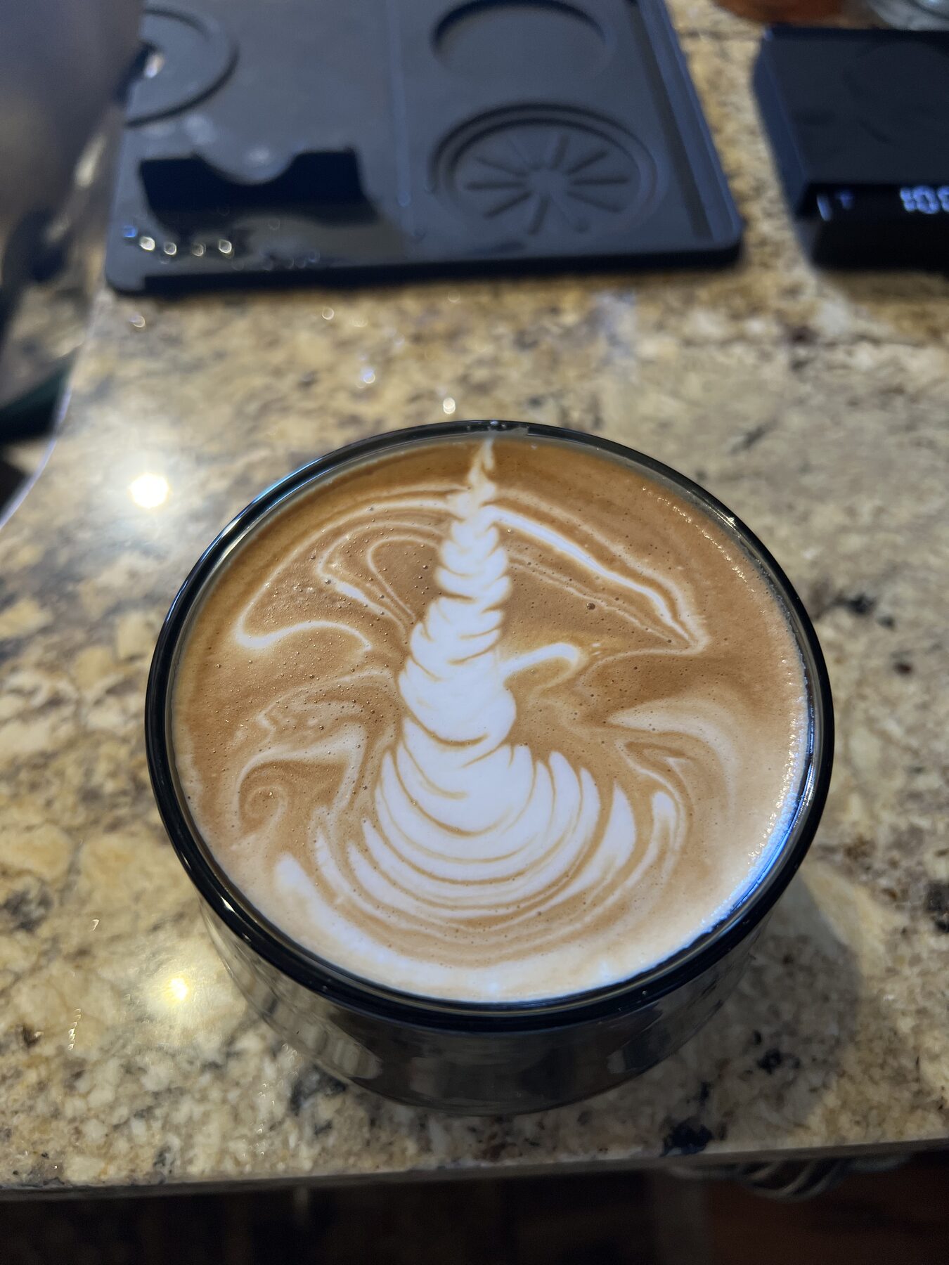 Wide feathered rosetta in a glass cup, tamper holder behind.