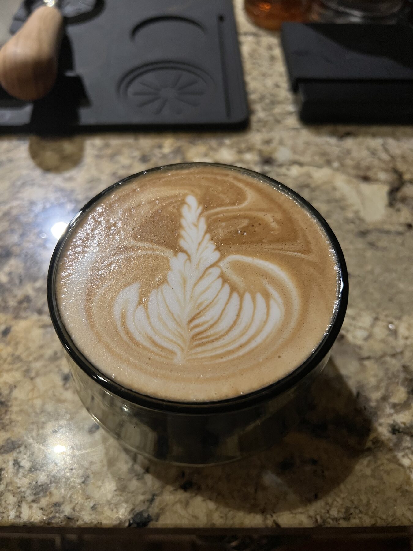 Crisp tulip latte art in a clear glass cup on granite, the kind of shot the controller is in service of.