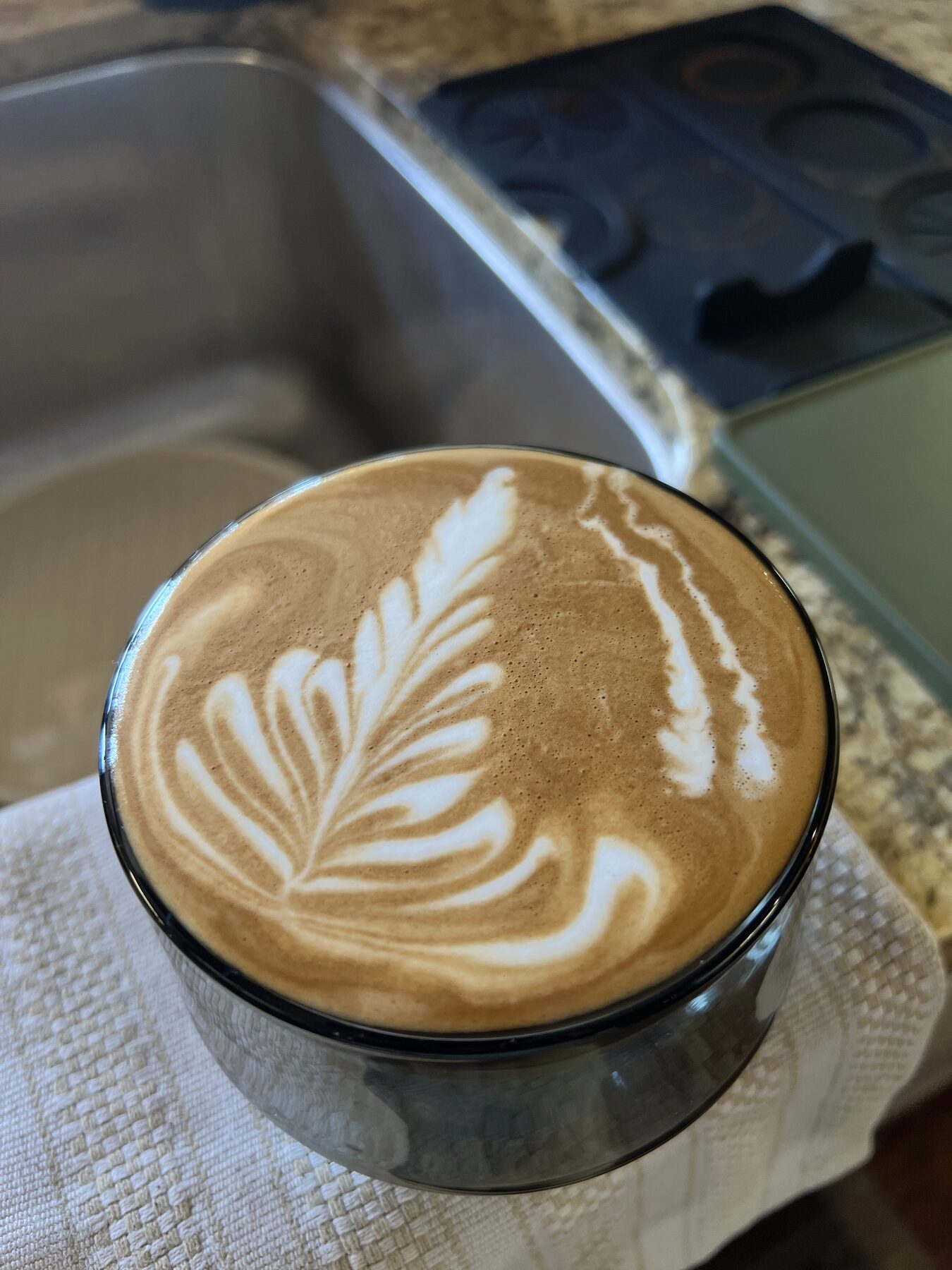 A finished latte in a glass on a countertop, seen from above, with poured leaf latte art.