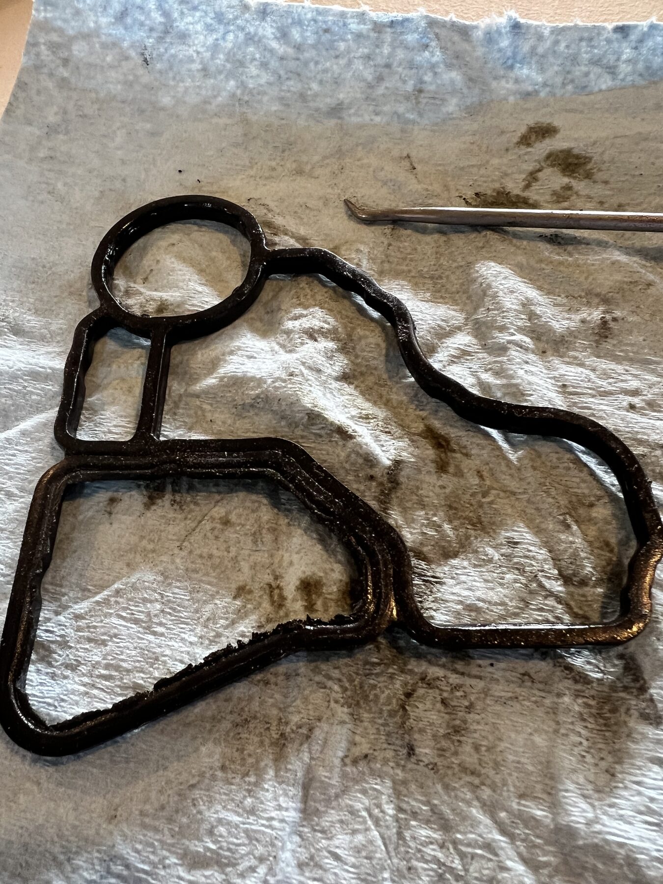 The old failed gasket on a paper towel, blackened, hardened, partially separated.