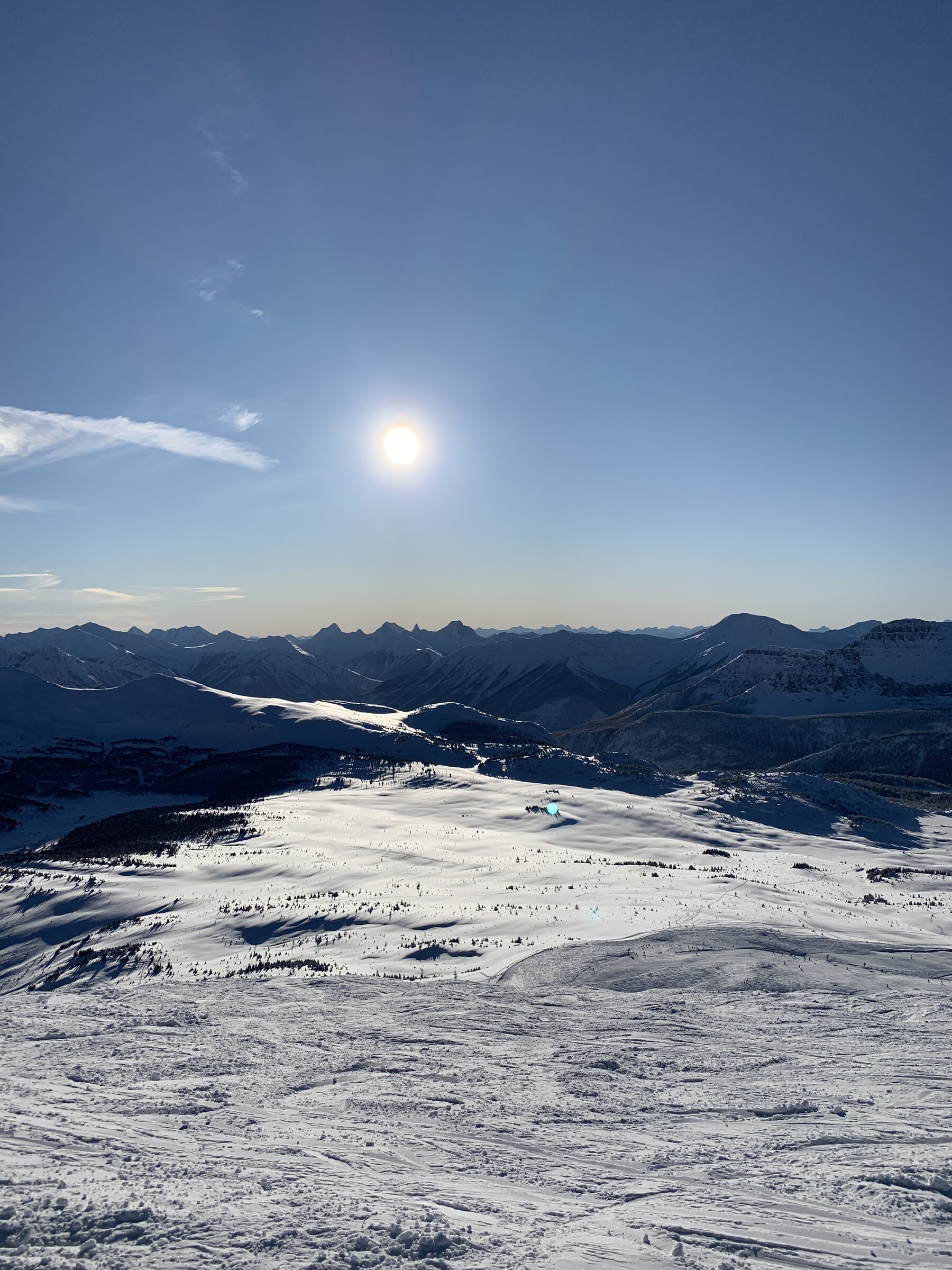 A skier standing at the top of a run in the Canadian Rockies, peaks and cloud behind.