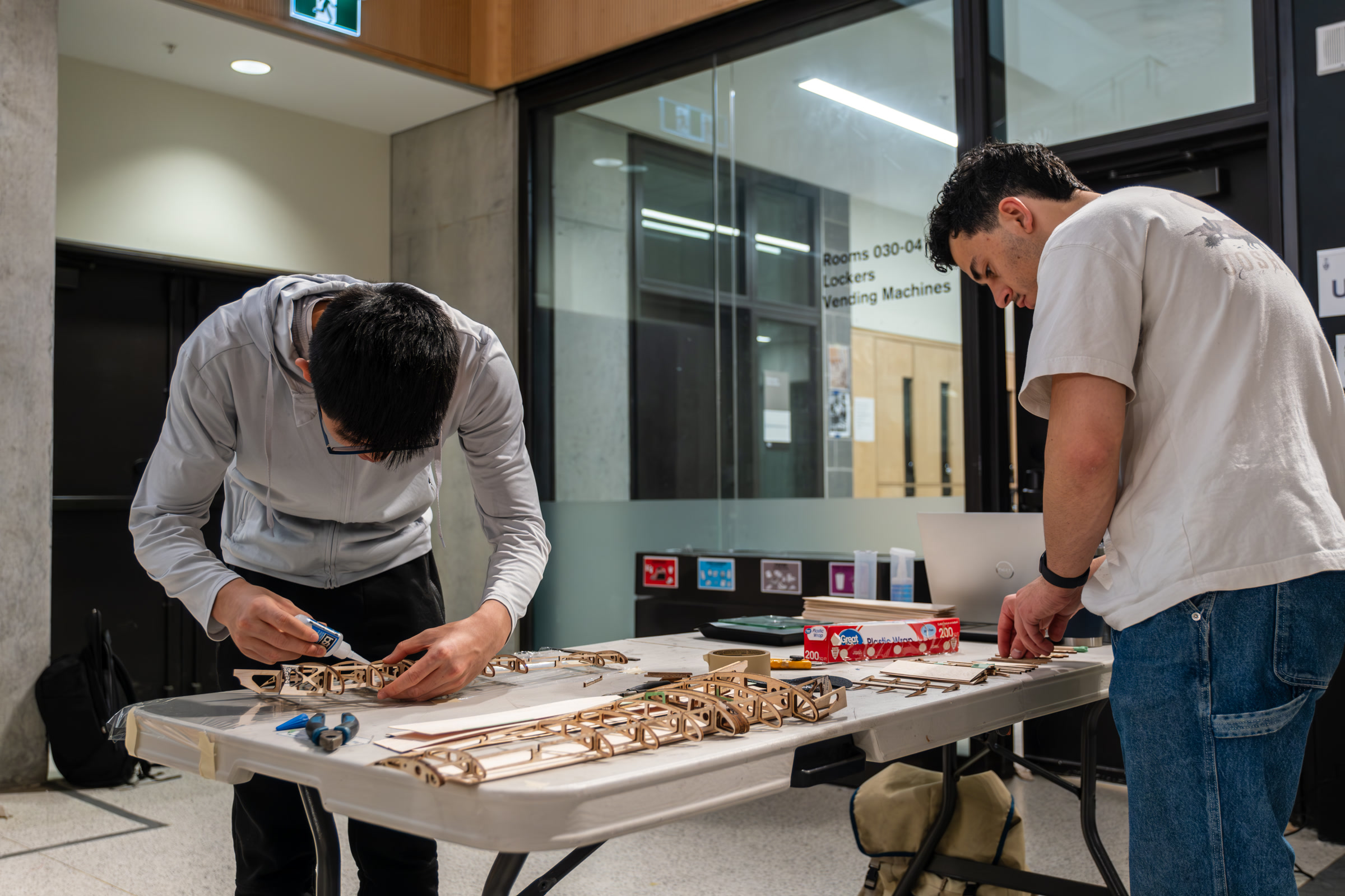 Two UTAT team members at a bench, mid-build on a wooden airframe