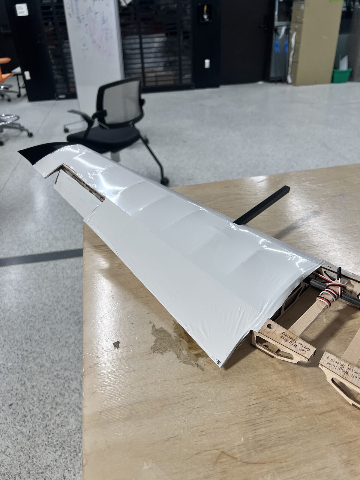 A covered competition wing lying on a workroom bench, servo and control linkage visible at the root.