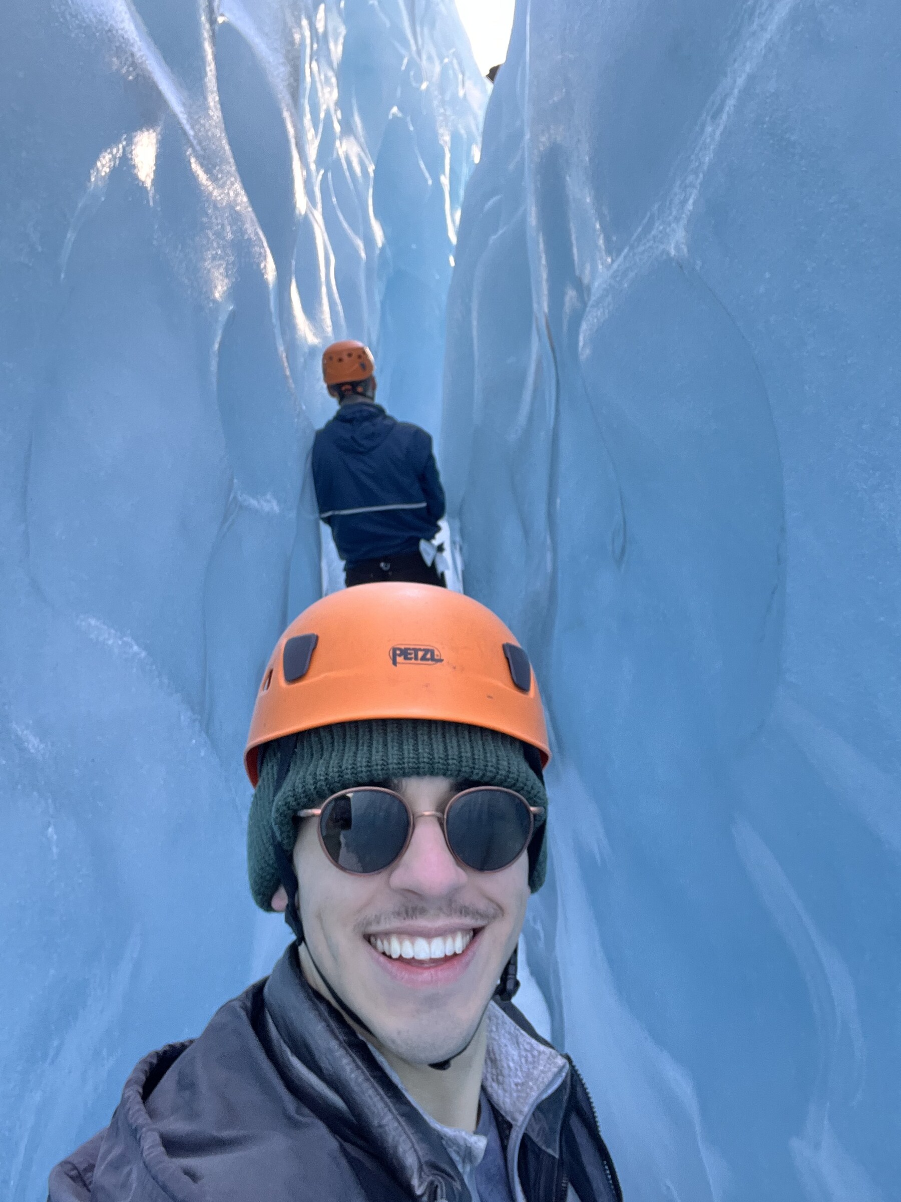 A figure standing in a narrow blue crevasse in a glacier, ice walls rising on both sides.