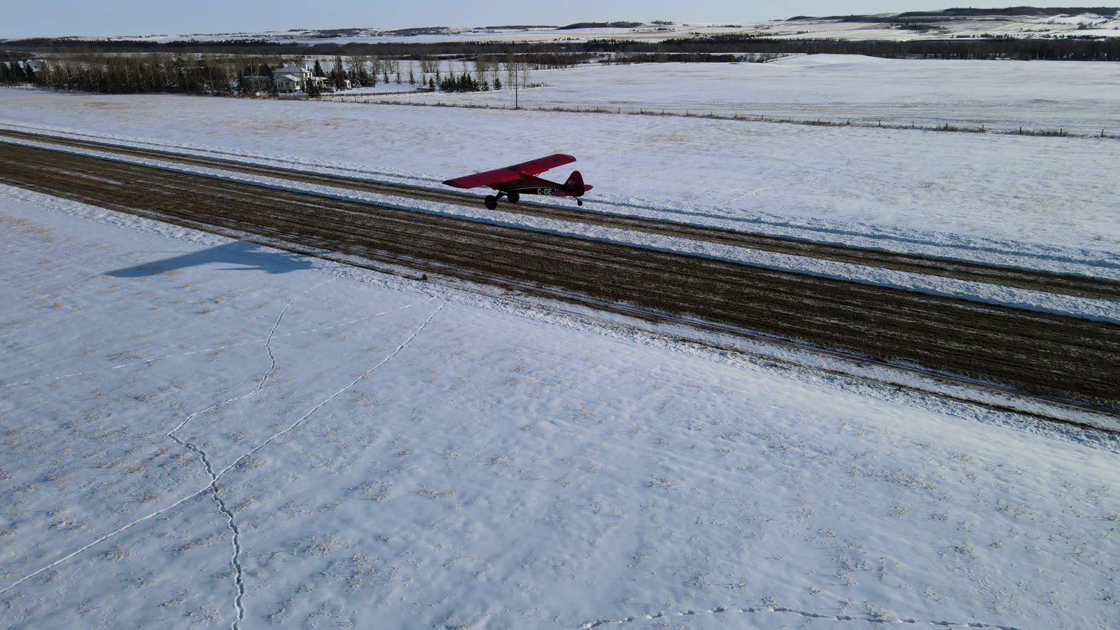 Red tailwheel aircraft on a snowy strip, aerial